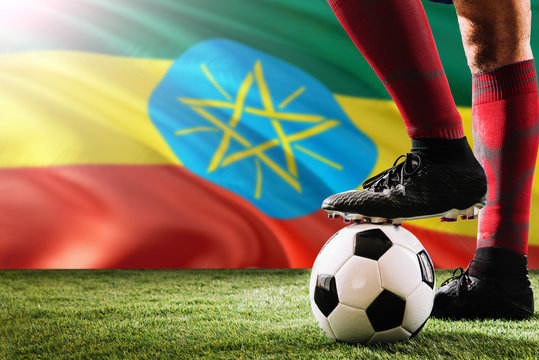 Close up legs of Ethiopia football team player in red socks, shoes on soccer ball at the free kick or penalty spot playing on grass.