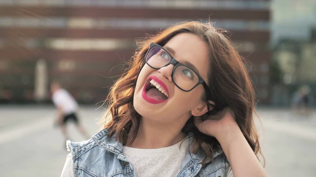 Charming young woman with a brown hair, gorgeous red lipstick and stylish look. Attractive young lady is laughing in the city-center, she turns to camera and smiles.