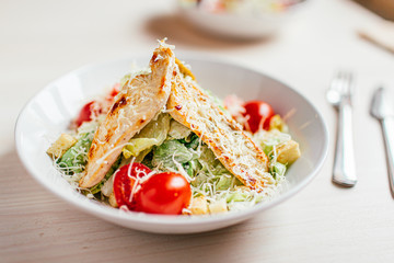 Fresh healthy caesar salad with chicken on white wooden table with fork and knife. Top view. Selective focus.