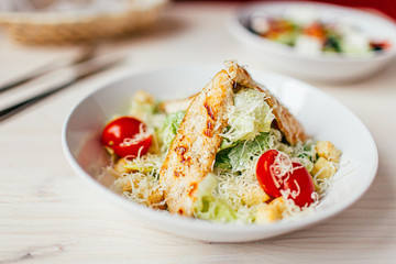 Fresh healthy caesar salad with chicken on white wooden table with fork and knife. Top view. Selective focus.
