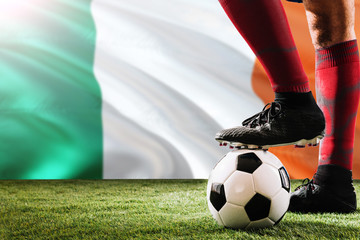 Close up legs of Ireland football team player in red socks, shoes on soccer ball at the free kick or penalty spot playing on grass.