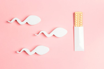 Female oral contraceptive pills blister in the way of sperm movement on pink background.