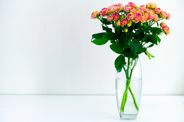 Bouquet of pink spray peony roses in vase on white table.