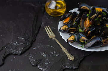Delicious cooked seafood mussels with herbs and olive oil on a white plate on black background. Mediterranean cuisine