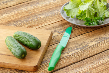 Just picked cucumbers lying on cutting board and leaves of salad on plate.