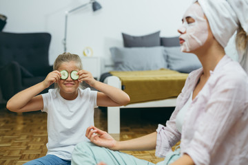 mother and daughter applying cosmetic face mask at home