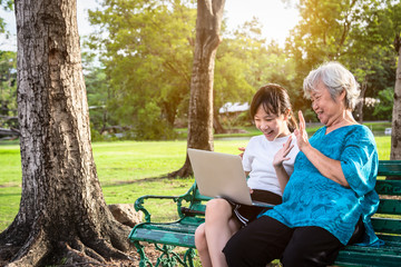 Happy asian granddaughter enjoy smiling and senior grandmother using video conferencing with laptop computer,child girl having video call,saying hi with their elderly woman in park,technology concept