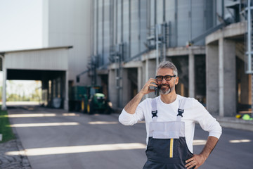 worker talking on mobile phone in front of grain silo outdoor © cherryandbees