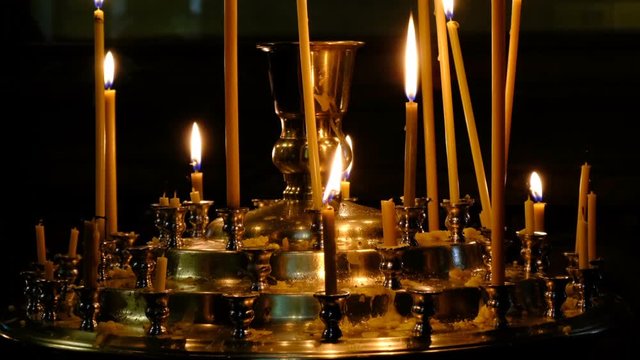 Subtle church candles burn in an Orthodox Christian church near holy images in the dark close-up, filmed using zooming and moving the camera