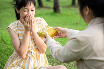 Happy asian family,mother giving surprise gift box and daughter was excited with gift box and smiling happily in summer,woman is congratulating her birthday,little child girl with parent in park
