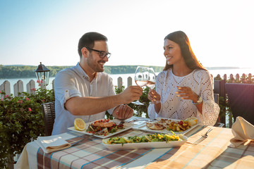Beautiful happy young couple making a toast, celebrating anniversary or birthday in a restaurant. Husband and wife having romantic dinner in a restaurant by the river