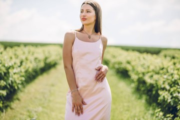 Fototapeta na wymiar Beautiful girl in pink dress walking in the field of currants