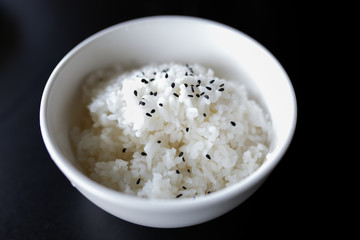 Japanese cooked rice in a white bowl on black table.