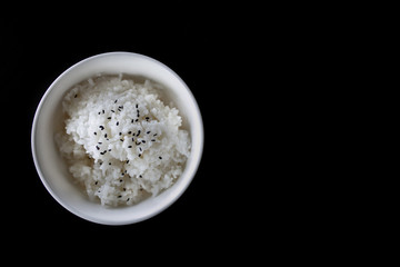 Japanese cooked rice in a white bowl on black table.