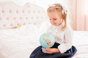 Little adorable blonde girl in school uniform and white golfs siting on a ber in her bedroom and shockes about first day in the school