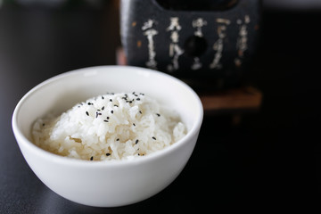 Japanese cooked rice in a white bowl on black table.