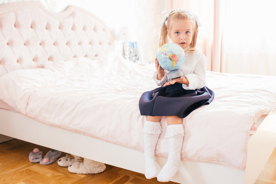 Little adorable blonde girl in school uniform and white golfs siting on a ber in her bedroom and shockes about first day in the school