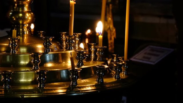 Subtle church candles burn in an Orthodox Christian church near holy images in the dark close-up, filmed using zooming and moving the camera