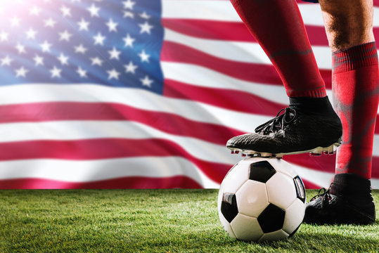 Close up legs of United States football team player in red socks, shoes on soccer ball at the free kick or penalty spot playing on grass.