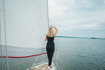 Blonde girl is on yacht bow. She look forward.