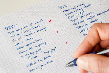 To do list. Concept of work/life balance. Close-up of a man's hand with  pen keeping track of a handwritten list of home and work-related tasks.
