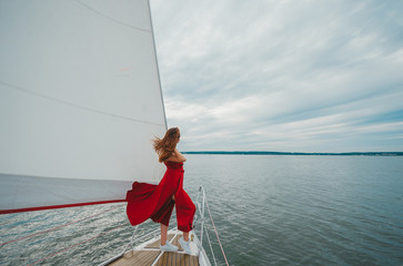 Beautiful young woman standing at front of private sailing yacht at sea.