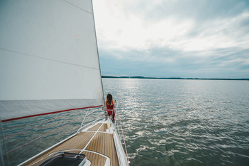 Beautiful female model in red dress standing on the deck of a yacht at sea.