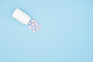Pills spilling out of pill bottle isolated on blue background. Top view with copy space. Medicine concept.