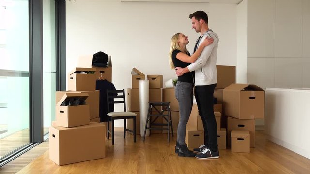 A happy moving couple hugs in a new apartment - piles of cardboard boxes in the background