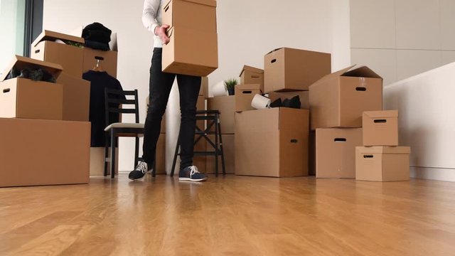 A moving man picks up a cardboard box and carries it away in an empty apartment - more boxes in the background