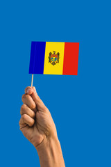 Woman hand holding Moldova flag with stick, waving flag on deep blue sky. National theme, deep blue sky.