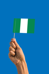 Woman hand holding Nigeria flag with stick, waving flag on deep blue sky. National theme, deep blue sky.