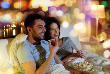 people, family and leisure concept - couple with popcorn watching tv at night at home