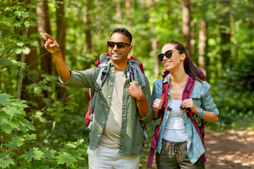 travel, tourism, hike and people concept - mixed race couple with backpacks in forest