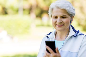 Fototapeta premium fitness, sport and healthy lifestyle concept - senior woman with earphones listening to music on smartphone at summer park