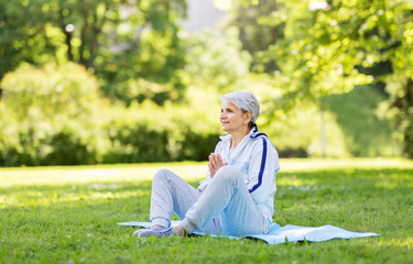 fitness, sport and healthy lifestyle concept - happy smiling senior woman doing yoga on exercise mat at summer park