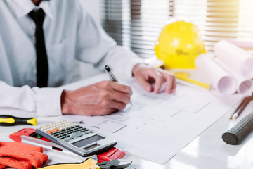 Close up Engineer calculator on office desk and engineer man working with blueprint.