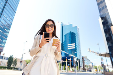 Fototapeta premium communication, lifestyle and technology concept - happy smiling young asian woman in sunglasses with takeaway coffee cup and smartphone on city street
