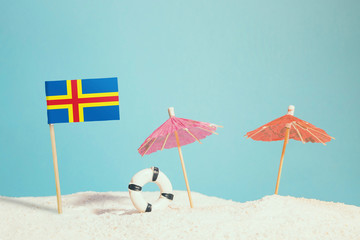 Miniature flag of Aland Islands on beach with colorful umbrellas and life preserver. Travel concept, summer theme.