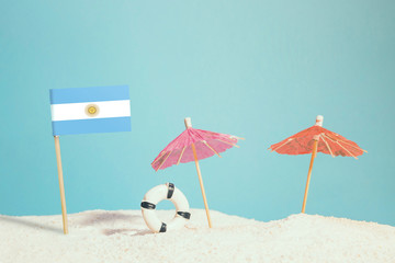 Miniature flag of Argentina on beach with colorful umbrellas and life preserver. Travel concept, summer theme.