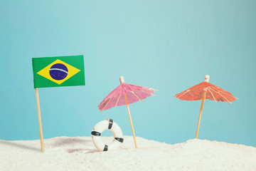 Miniature flag of Brazil on beach with colorful umbrellas and life preserver. Travel concept, summer theme.