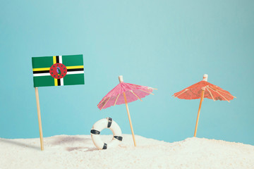 Miniature flag of Dominica on beach with colorful umbrellas and life preserver. Travel concept, summer theme.