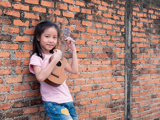 Little asian child play the ukulele, old brick wall background