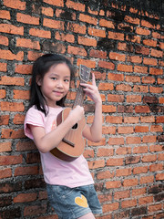 Little asian child play the ukulele, old brick wall background