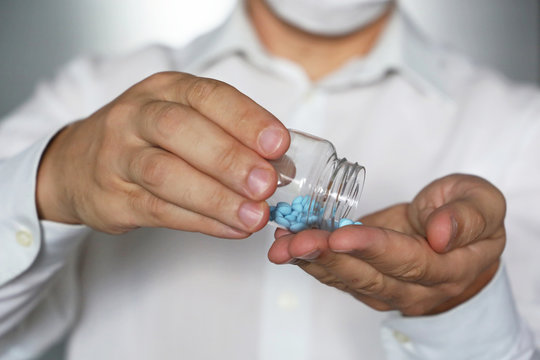 Doctor giving pills, physician in medical mask holding in hands bottle with blue tablets. Concept of dose of drugs, vitamins, viagra, pharmacy, anti-inflammatory