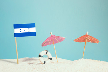 Miniature flag of Honduras on beach with colorful umbrellas and life preserver. Travel concept, summer theme.