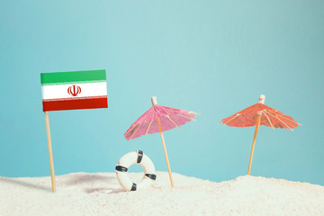 Miniature flag of Iran on beach with colorful umbrellas and life preserver. Travel concept, summer theme.