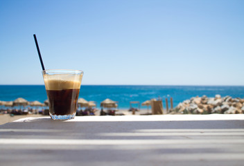 glass with ice coffee fredo espresso or frappe on the corner of the table with beach on background