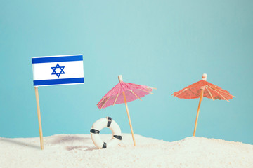 Miniature flag of Israel on beach with colorful umbrellas and life preserver. Travel concept, summer theme.