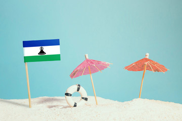 Miniature flag of Lesotho on beach with colorful umbrellas and life preserver. Travel concept, summer theme.